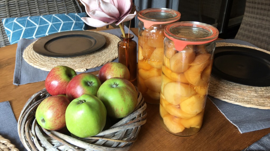 Eingemachte Äpfel neben einem Korb mit frischen Äpfeln