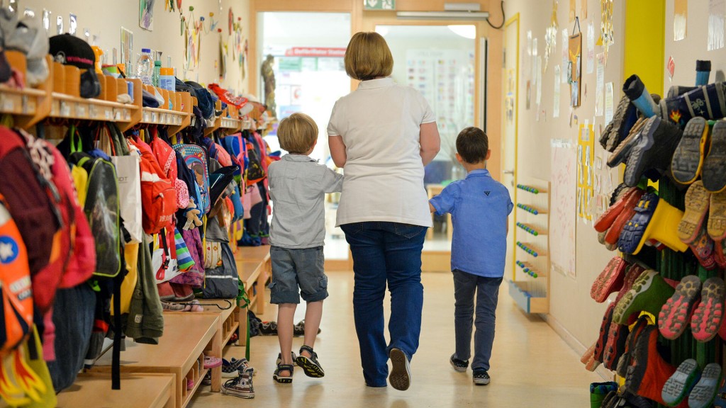 Eine Erzieherin führt zwei Kinder über den Flur einer Kintertagesstätte