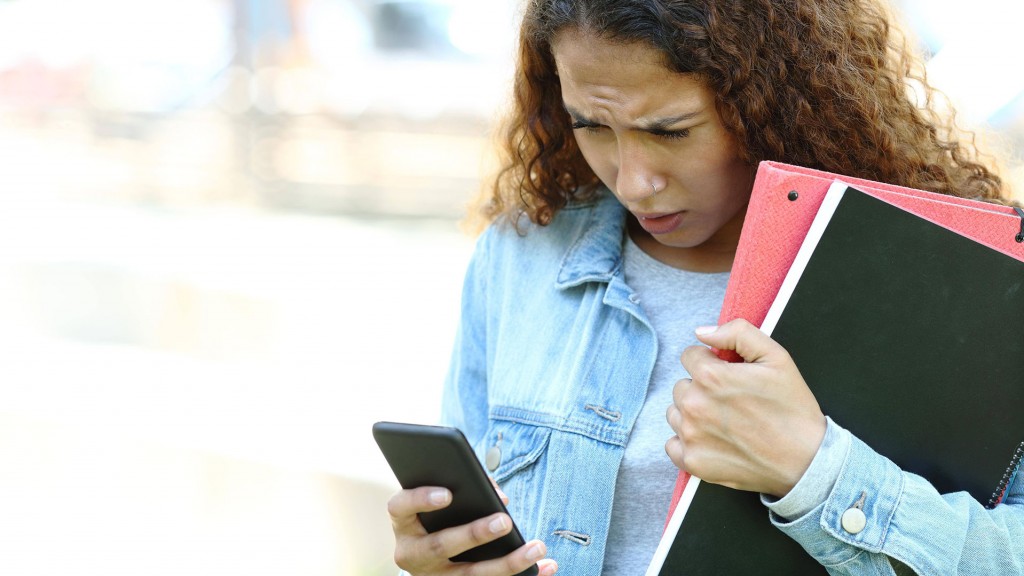 Eine jugendliche Schülerin schaut mit Stirnrunzeln auf ihr Smartphone