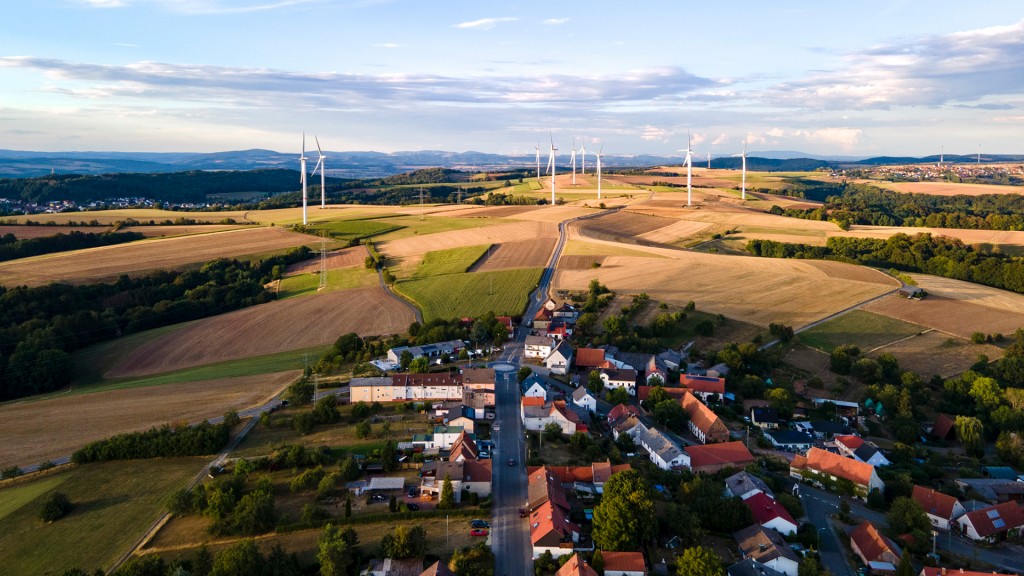 Windkraftanlagen stehen nahe einem Dorf auf einer Anhöhe