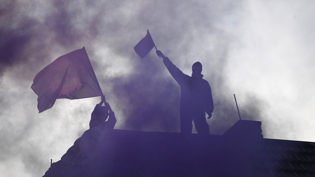 Männer stehen nach einer Demonstration mit Fahnen auf einem Hausdach.