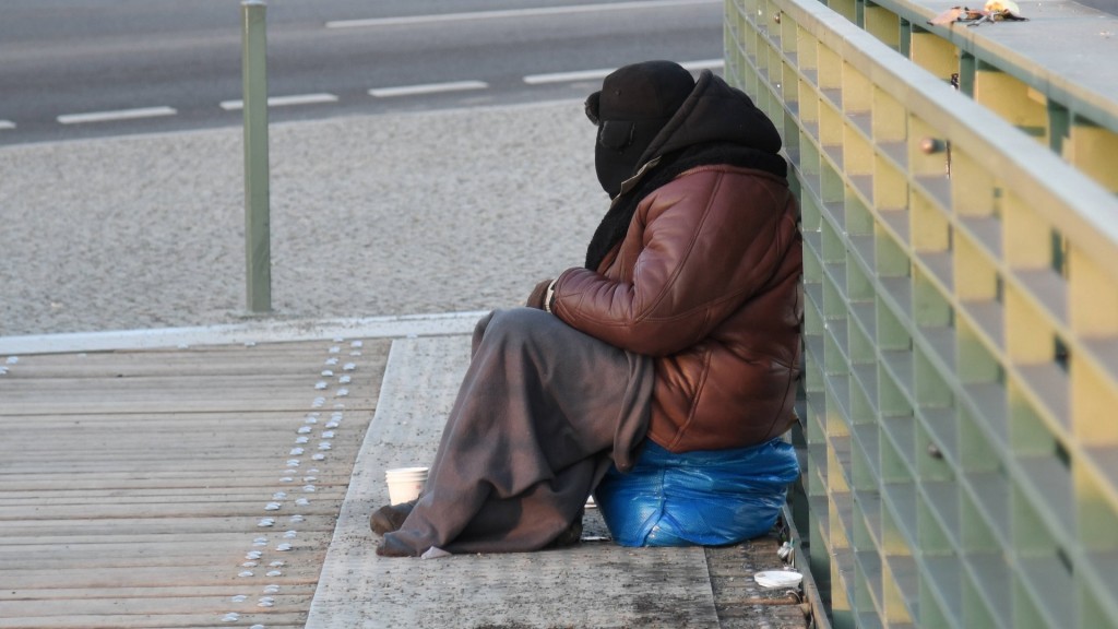 Ein Obdachloser, eingemummt in eine dicke Jacke, Mütze und Decke, sitzt bei bissiger Kälte im Freien.