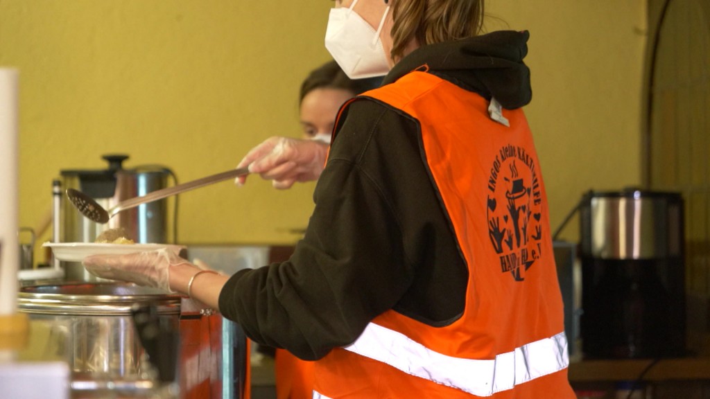 Eine Frau serviert Essen in einer Küche für obdachlose Menschen