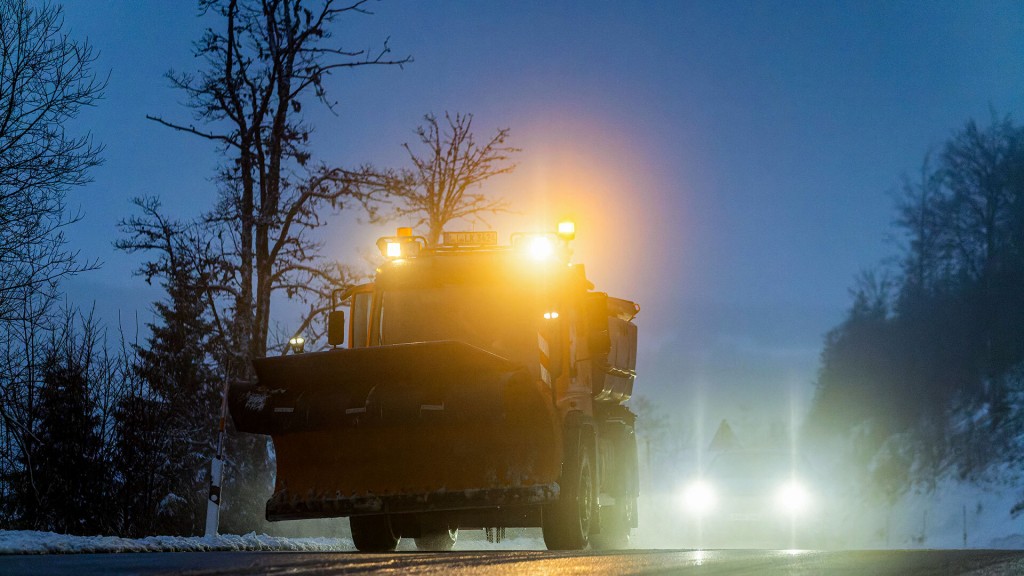 Ein Auto fährt in der Dämmerung hinter einem Räumfahrzeug des Winterdienstes