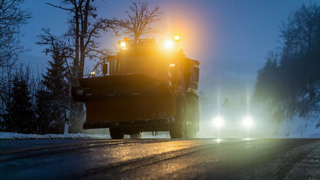 Ein Auto fährt in der Dämmerung hinter einem Räumfahrzeug des Winterdienstes