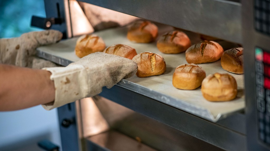 Ein Bäcker zieht ein Blech mit Brötchen aus dem Ofen