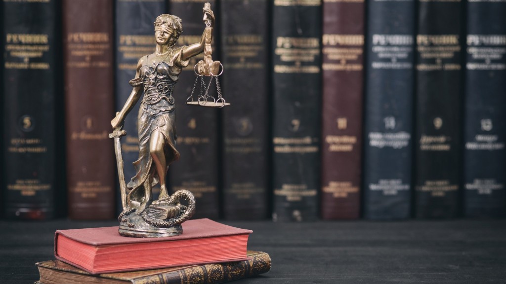 Eine Statuette der Justitia steht vor alten Gesetzbüchern