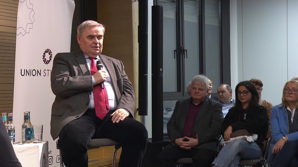 Foto: Peter Müller sitzt mit Mikrofon auf einem Stuhl vor Publikum