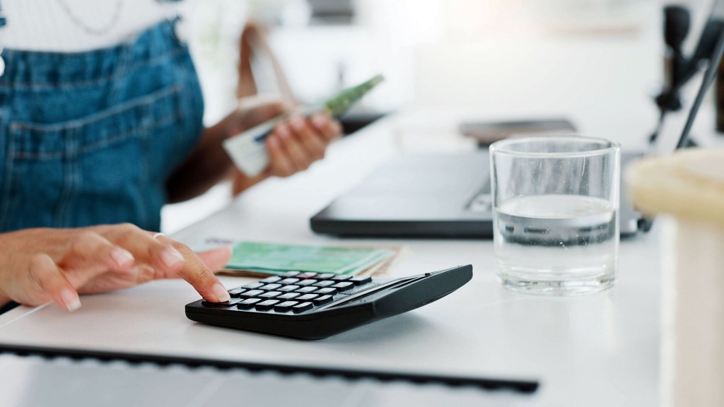 Eine Frau sitzt am Tisch mit Geldscheinen in der Hand und tippt auf einen Taschenrechner