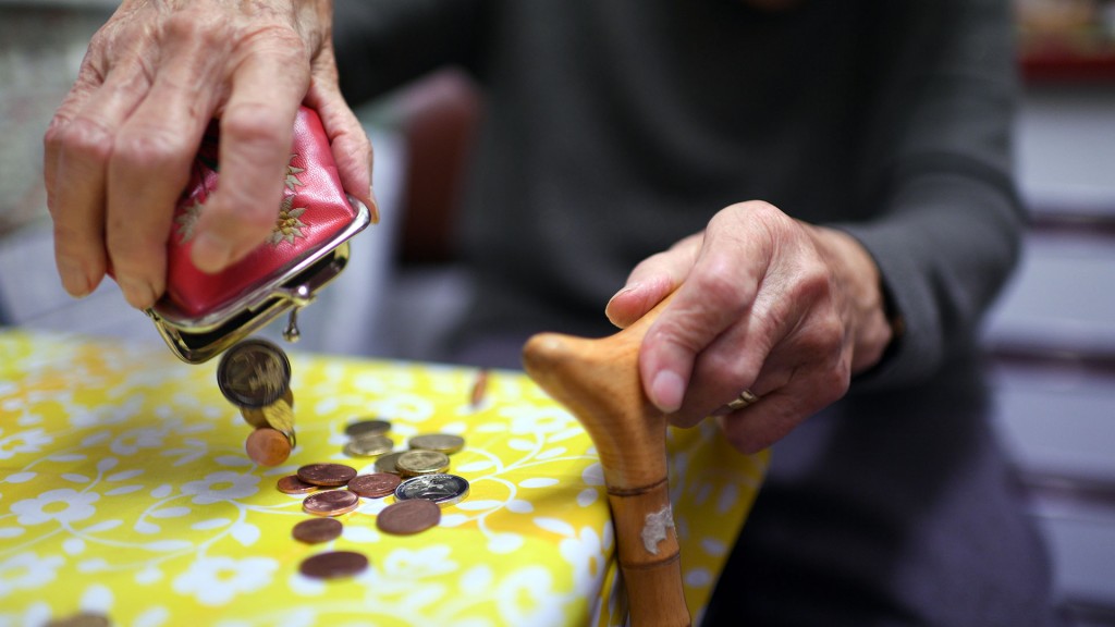 Eine Seniorin schüttet Münzen aus ihrem Geldbeutel auf den Küchentisch