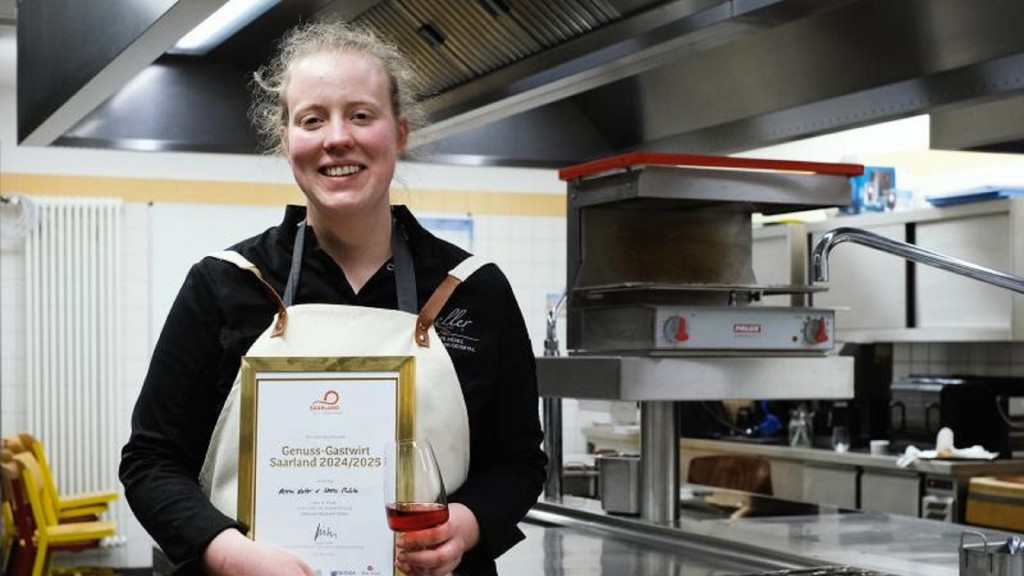 Anna Keller steht in einer Küche und hält die Auszeichnung zur Genuss-Gastwirtin 2024 in ihren Händen.