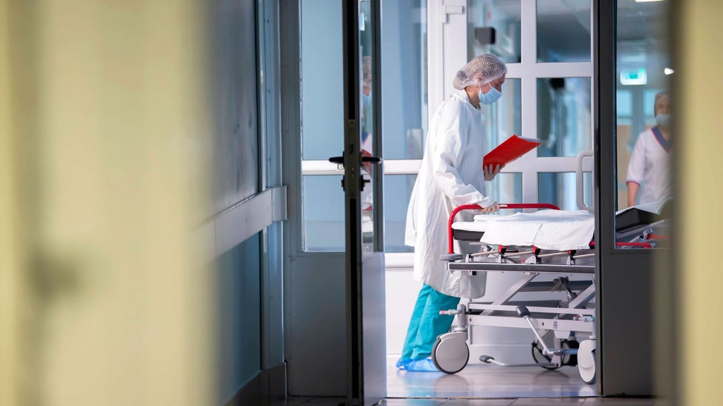 Krankenhausmitarbeiterin schiebt ein leeres Patientenbett über den Flur