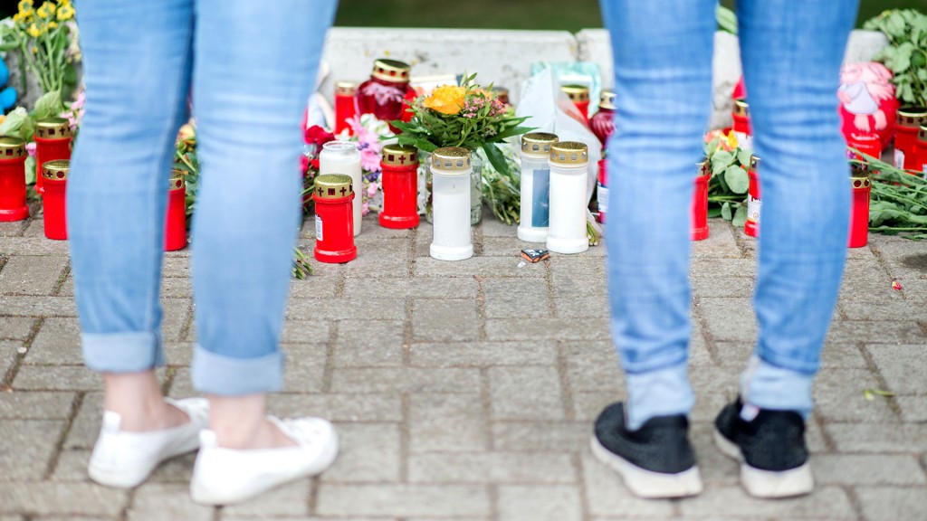 Foto: Zwei Frauen stehen zur Andacht vor Kerzen und Blumen an einem Tatort