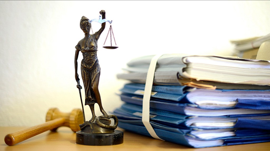 Foto: Nachbildung der Justitia neben einem Aktenstapel 