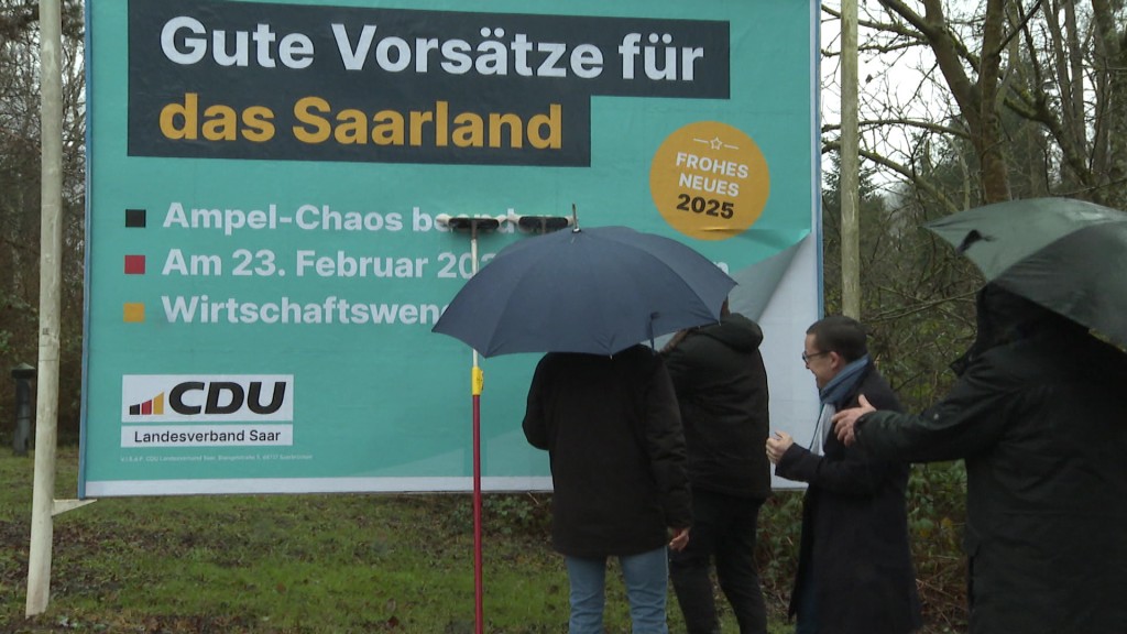 Foto: Menschen vor einem Wahlplakat der CDU