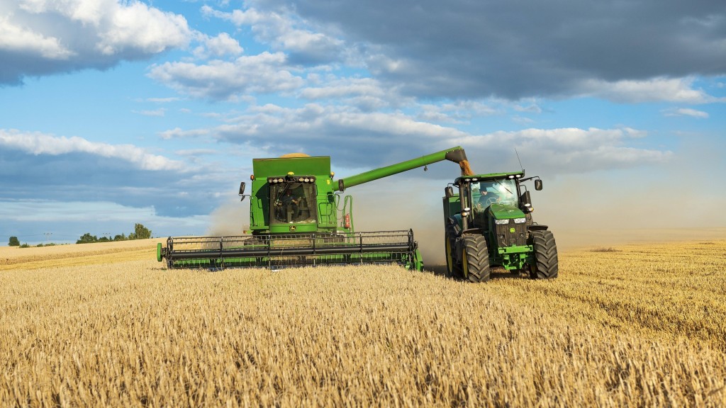 Mähdrescher erntet Weizen und entlädt Getreide auf einen Traktor mit Anhänger.