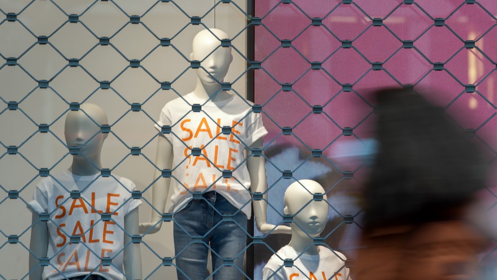 Hinter geschlossenen Sicherheitsgittern stehen Schaufensterpuppen mit Sale-T-Shirts