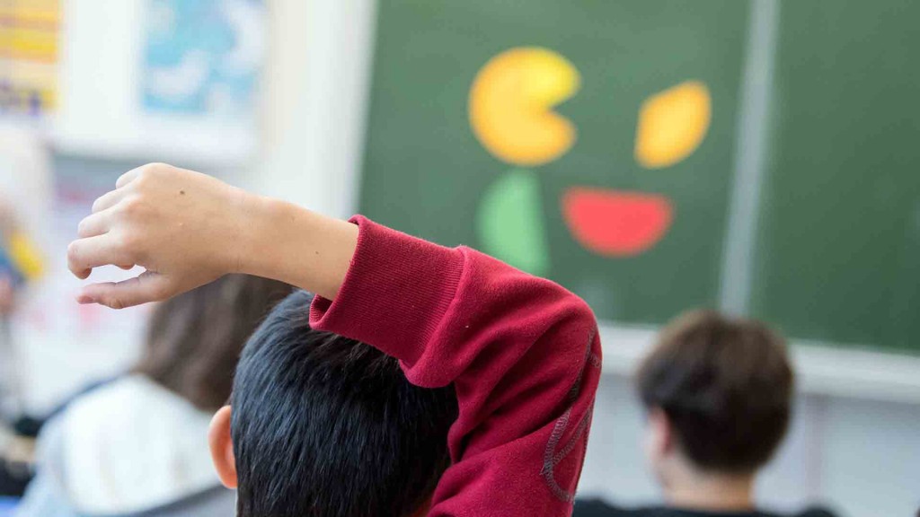 Foto: Ein Junge sitzt mit dem Arm überm Kopf in einer Grundschulklasse