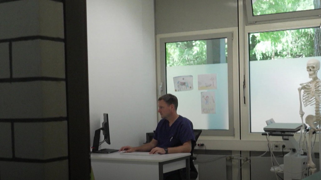 Foto: Arzt sitzt am Schreibtisch in einem Behandlungszimmer 