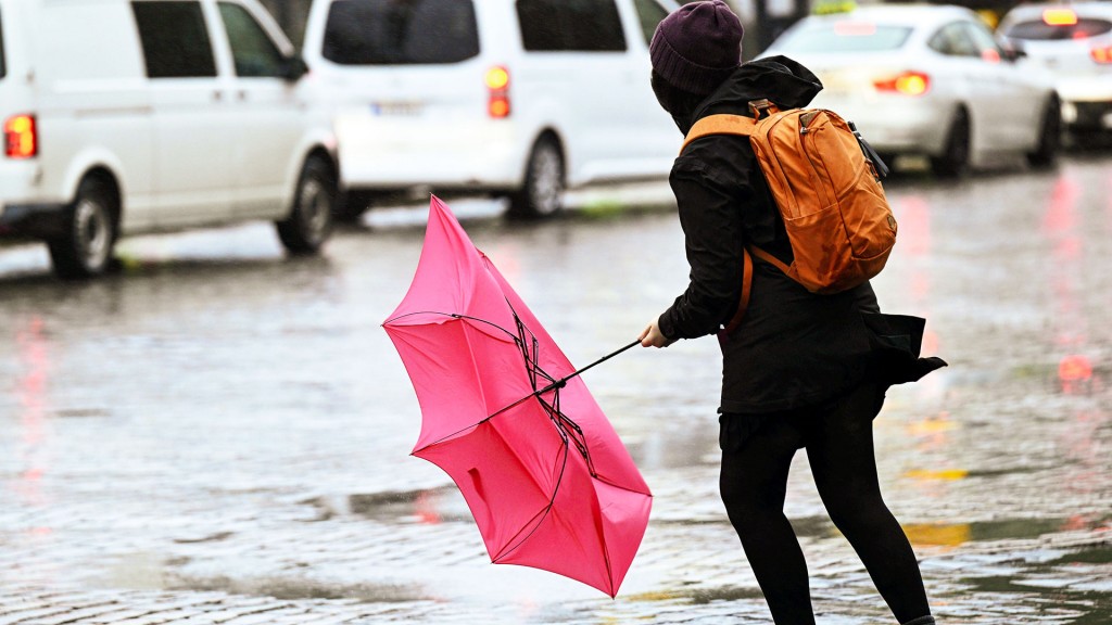 Eine Frau kämpft mit ihrem Regenschirm, der von einer Windböe bei Regen erfasst wird