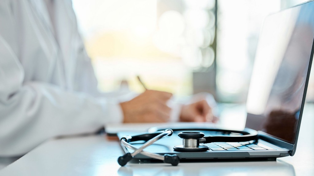 Ein Stethoskop liegt auf dem Computer eines Arztes im Hintergrund