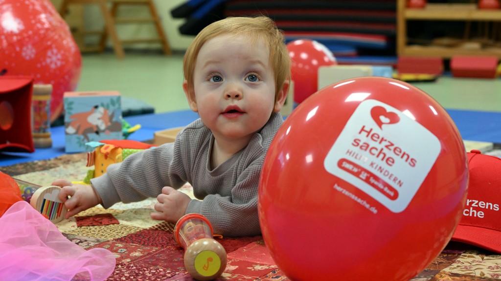 Ein Kleinkind spielt auf dem Boden vor einem Herzenssache-Luftballon