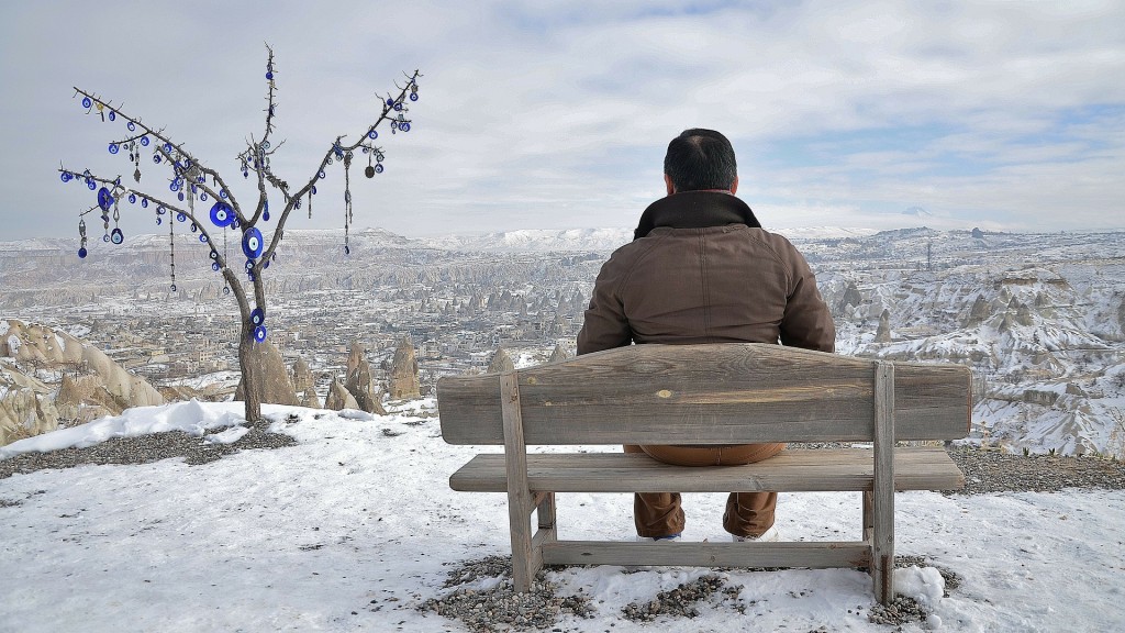 Ein Mann sitzt auf einer Holzbank und blickt über Hügel und Wälder zum Horizont
