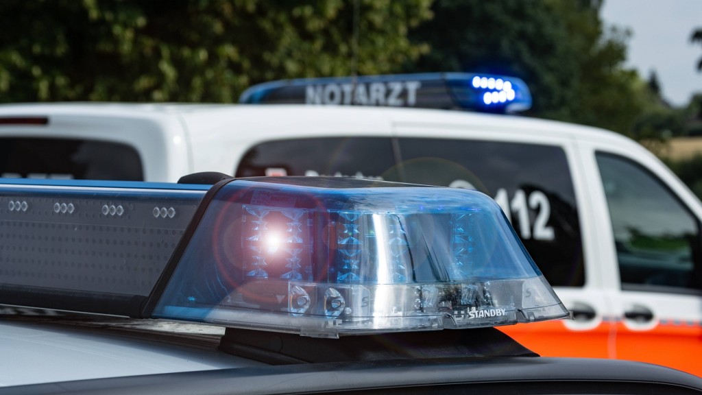 Foto: Ein Einsatzfahrzeug, Streifenwagen, der Polizei steht mit Blaulicht an einem Unfallort, im Hintergrund sieht man Rettungsfahrzeug mit der Aufschrift Notarzt. 