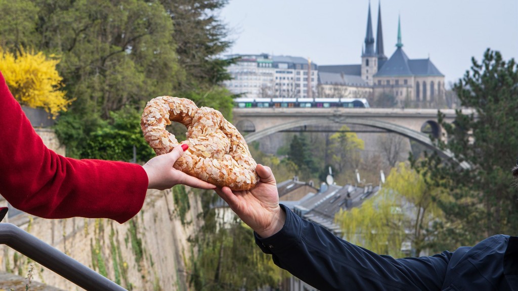 Ein Mann reicht einer Frau eine Brezel vor der Kulisse von Luxemburg