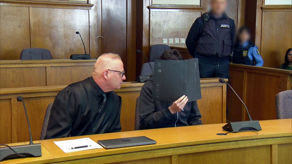 Foto: Landgericht Saarbrücken. Der Angeklagte sitzt neben seinem Anwalt und verdeckt sein Gesicht mit einer Mappe.