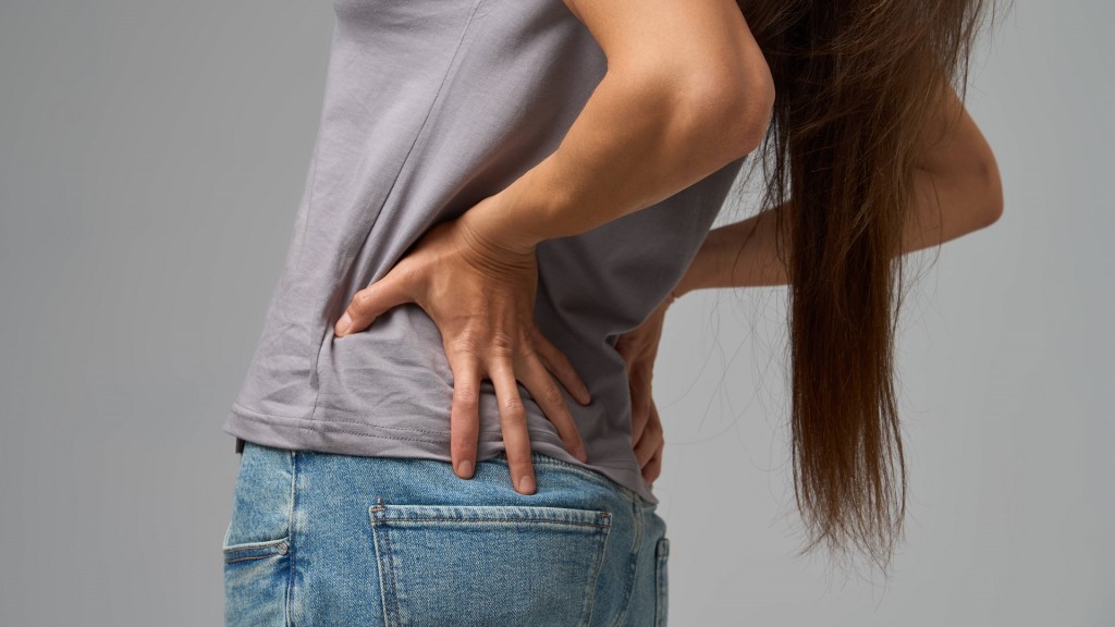 Nahaufnahme der Hände einer Frau, die sich vor Schmerzen den unteren Rücken hält