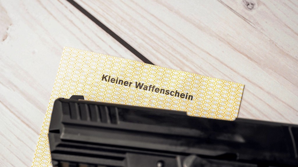 Ein kleiner Waffenschein liegt auf einem Tisch unter dem Lauf einer Pistole