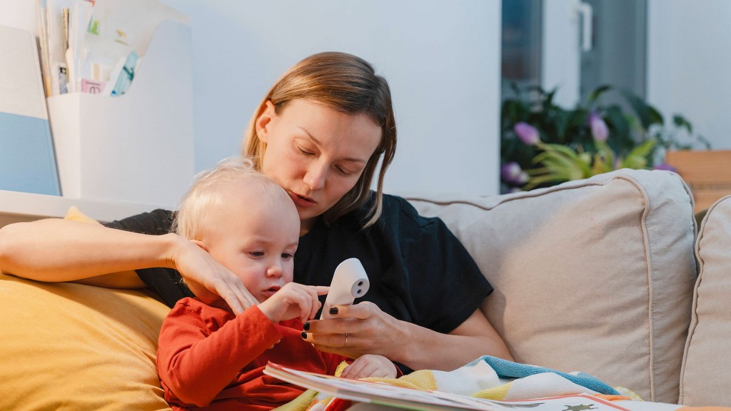 Eine Frau sitzt mit Kleinkind und Fieberthermometer auf einer Couch
