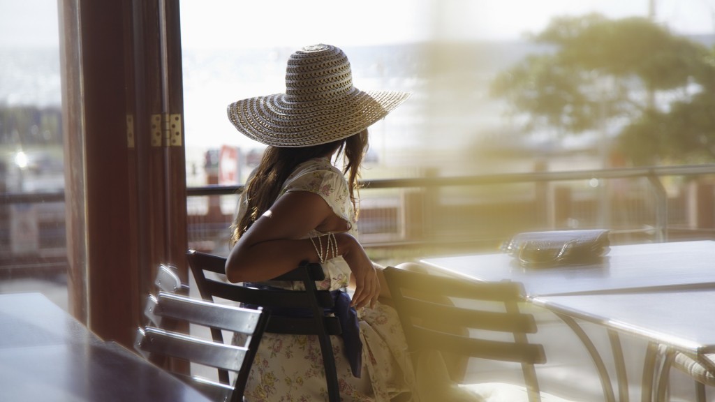Eine junge Frau mit Sonnenhut sitzt wartend in einem Café