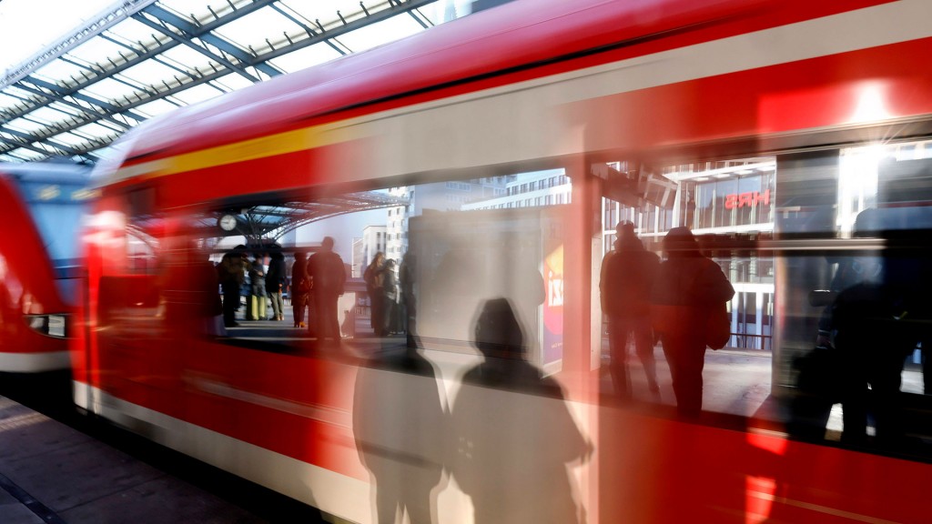 Schatten von wartenden Fahrgästen am Gleis fallen auf eine einfahrenden Regionalbahn