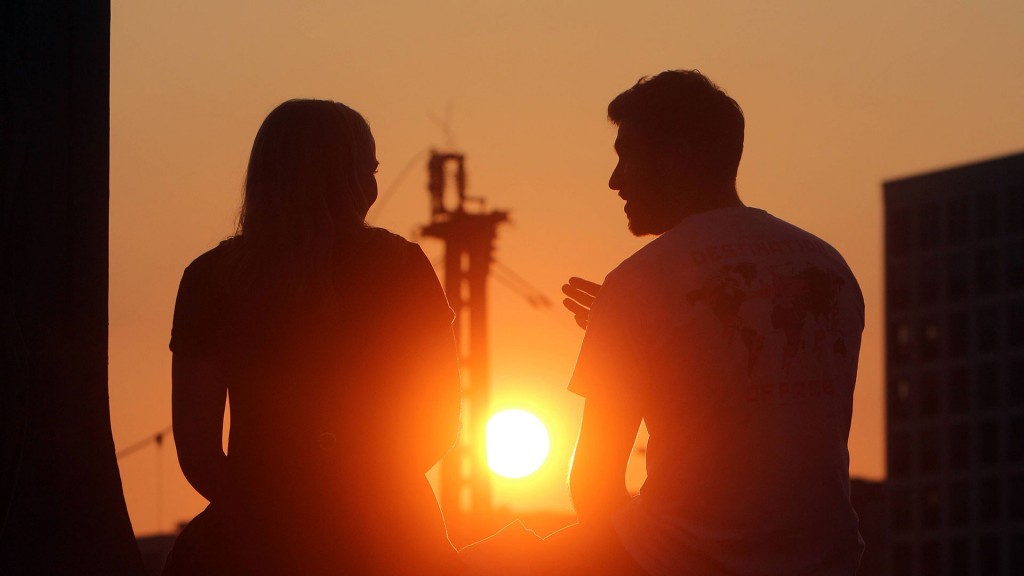 Junge Leute sitzen auf dem Geländer einer Brücke und genießen den Sonnenuntergang