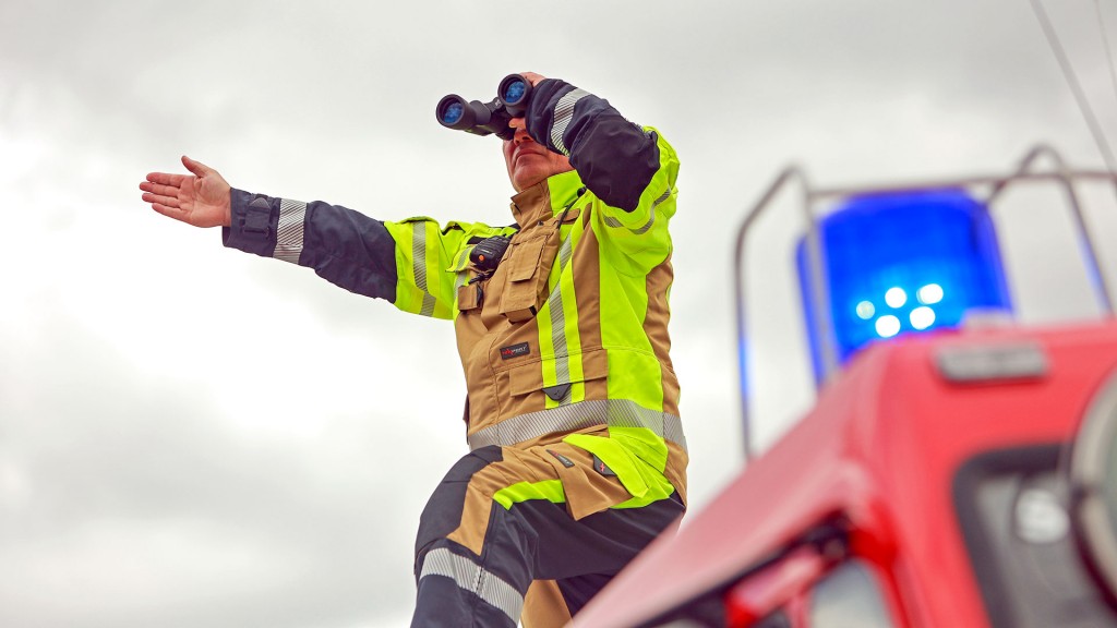 Ein Feuerwehrmann steht mit Fernglas auf dem Dach eines Einsatzfahreuges.