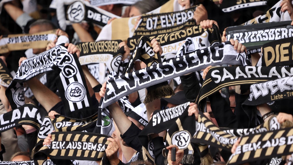 Fans der SV 07 Elversberg halten auf der Tribüne ihre Schals hoch