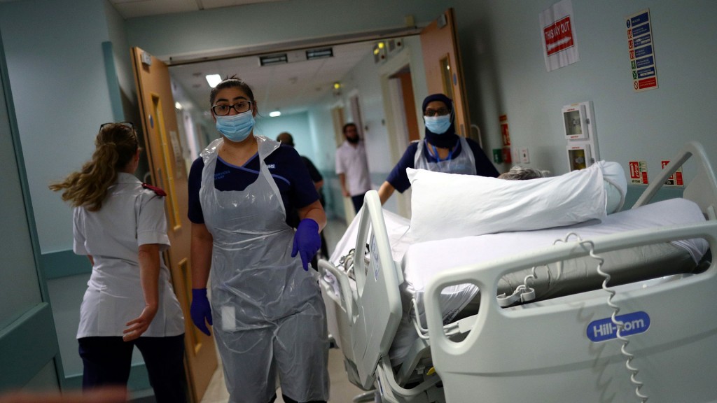 Foto: Medizinische Mitarbeiter in Schutzkleidung schieben einen Patienten auf einem Krankenhausbett durch einen Korridor