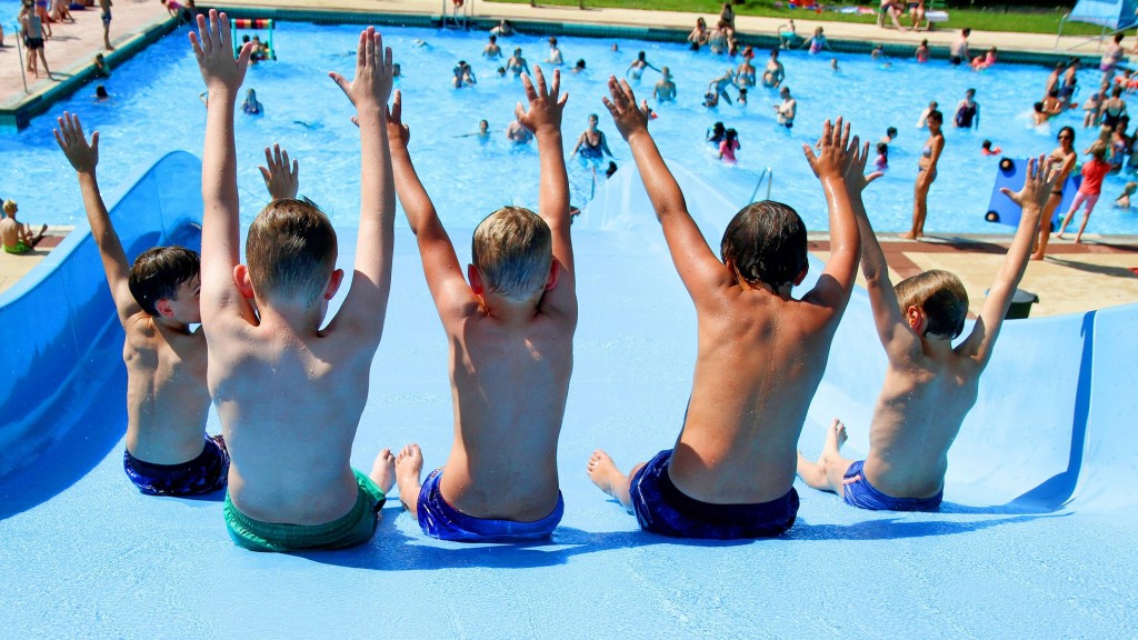 Badespaß im Schwimmbad. Bei Hitze springen Kinder von einer Rutsche in das blaue Wasser.