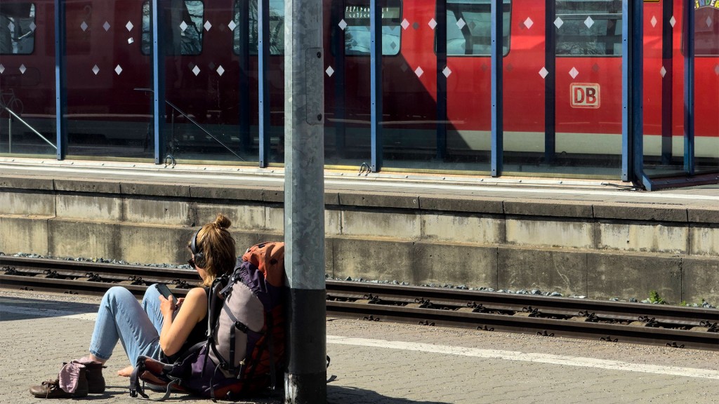 Eine Rucksacktouristin sitzt auf dem Boden und wartet auf den Zug.