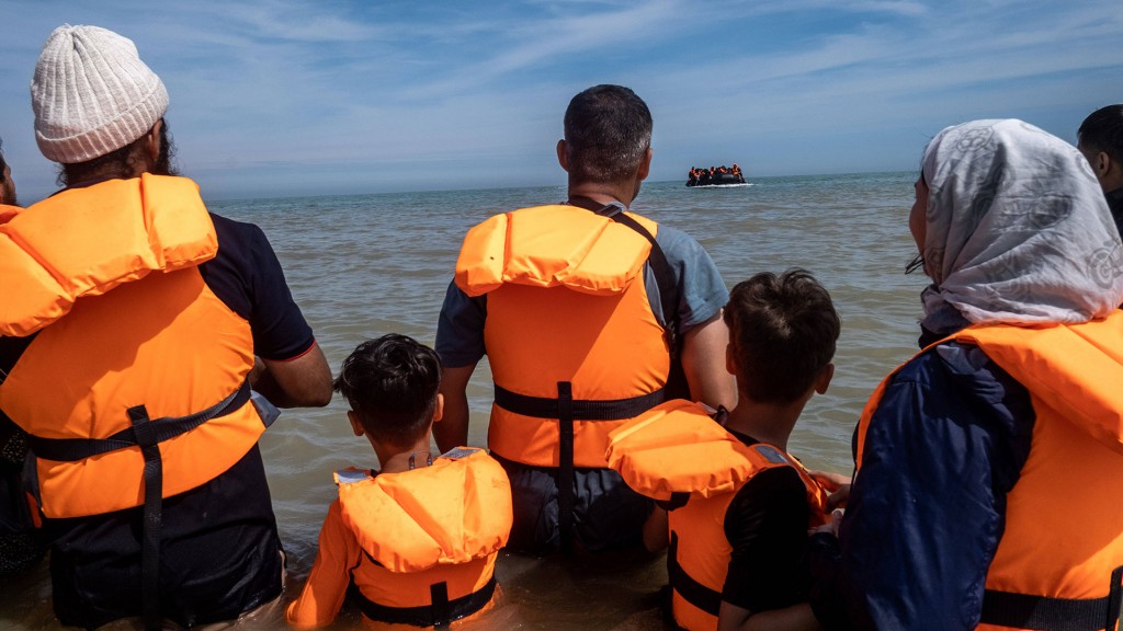 Foto: Eine Gruppe Asyl-Suchender wartet am Strand auf ein Boot