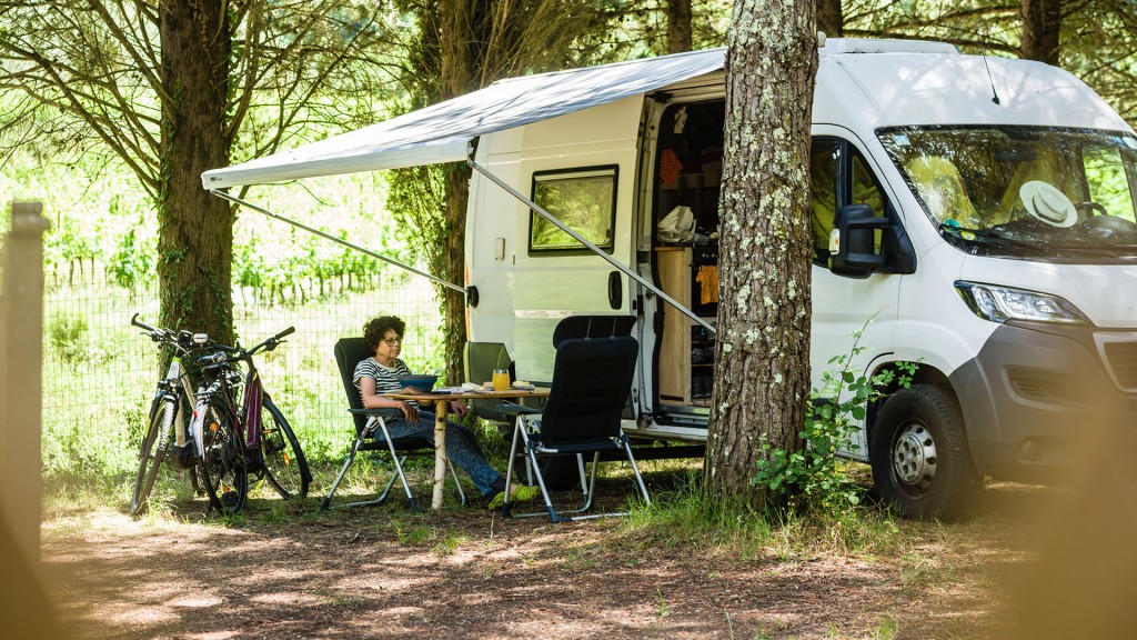 Ein Camper mit Markise und Campingmöbeln steht auf einem Stellplatz für Wohnmobile zwischen Bäumen
