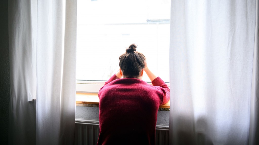 Foto: Eine Frau sitzt mit Kopf in den Händen am Fenster