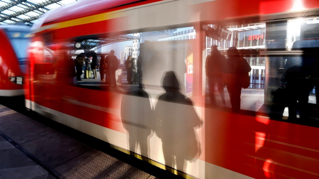 Foto: Schatten von wartenden Fahrgästen am Gleis fallen auf eine einfahrenden Regionalbahn