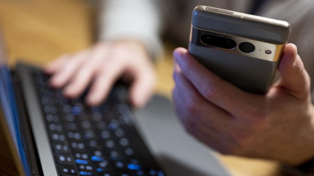 Ein Mann sitzt am Laptop und hat sein Handy gleichzeitig in der Hand