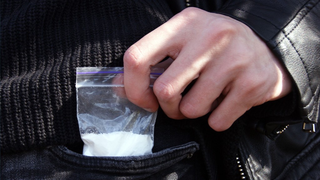 Foto: Eine Person holt ein kleines Plastiktütchen mit weißem Pulver aus einer Hosentasche.