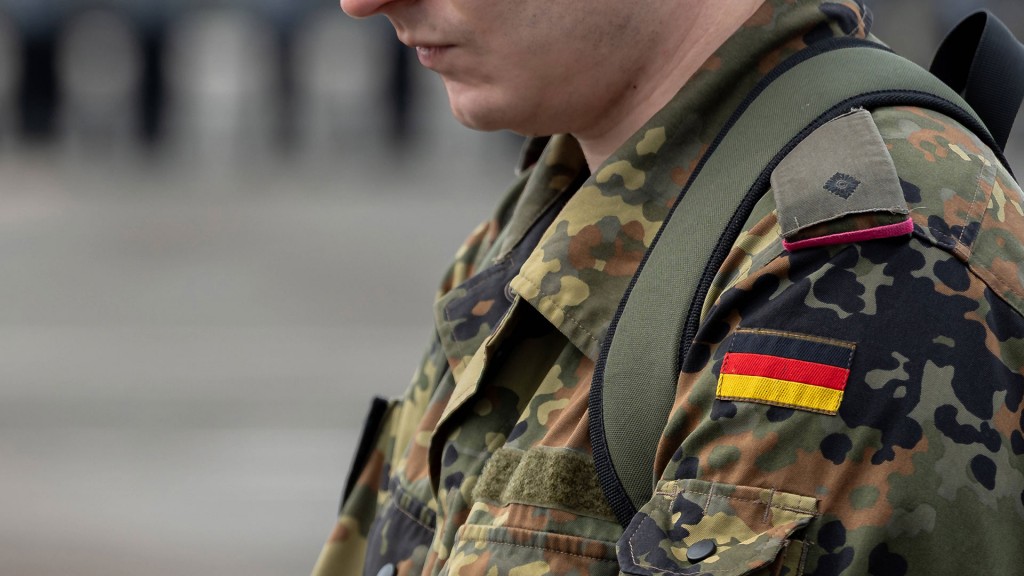 Ein junger Bundeswehrsoldat in Flecktarn-Uniform mit dem deutschen Hoheitsabzeichen auf der Schulter blickt nach unten.
